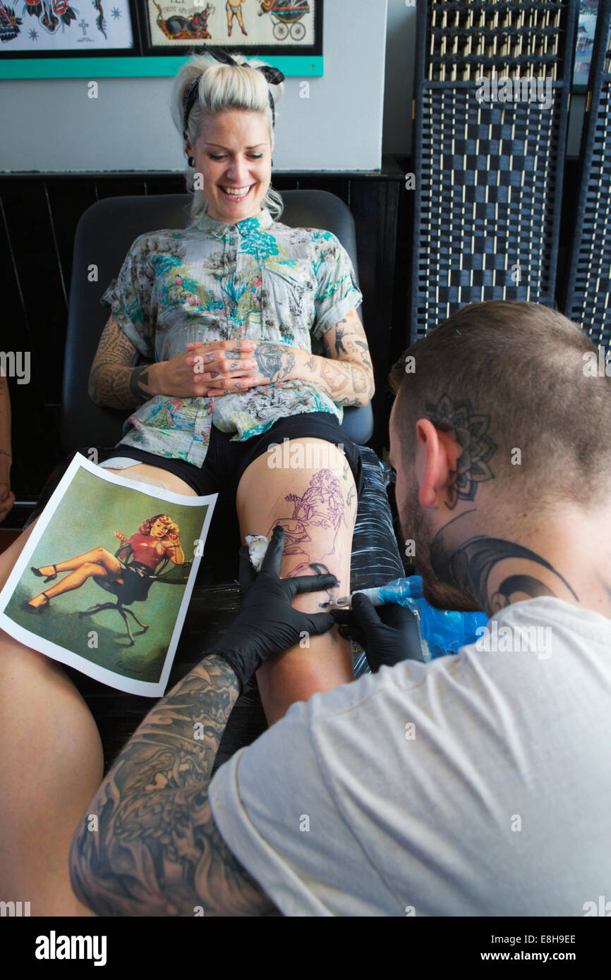 London salotto tattoo: giovani donne avente la sua gamba tatuato. Tattooist mediante tatuaggio pistola, copia di design da un'immagine. Foto Stock