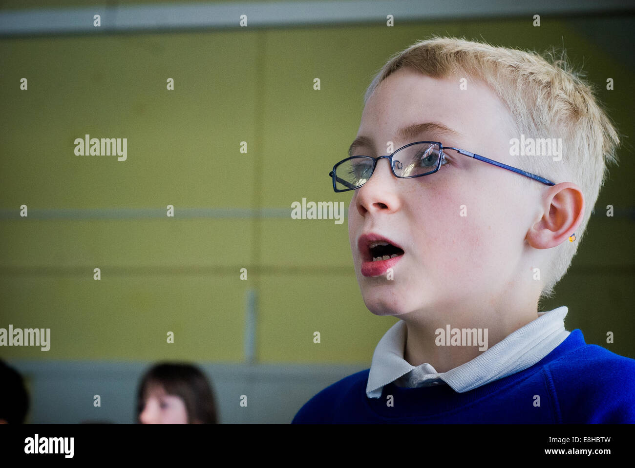 Ragazzo con gli occhiali canto presso una scuola primaria di assemblaggio, REGNO UNITO Foto Stock