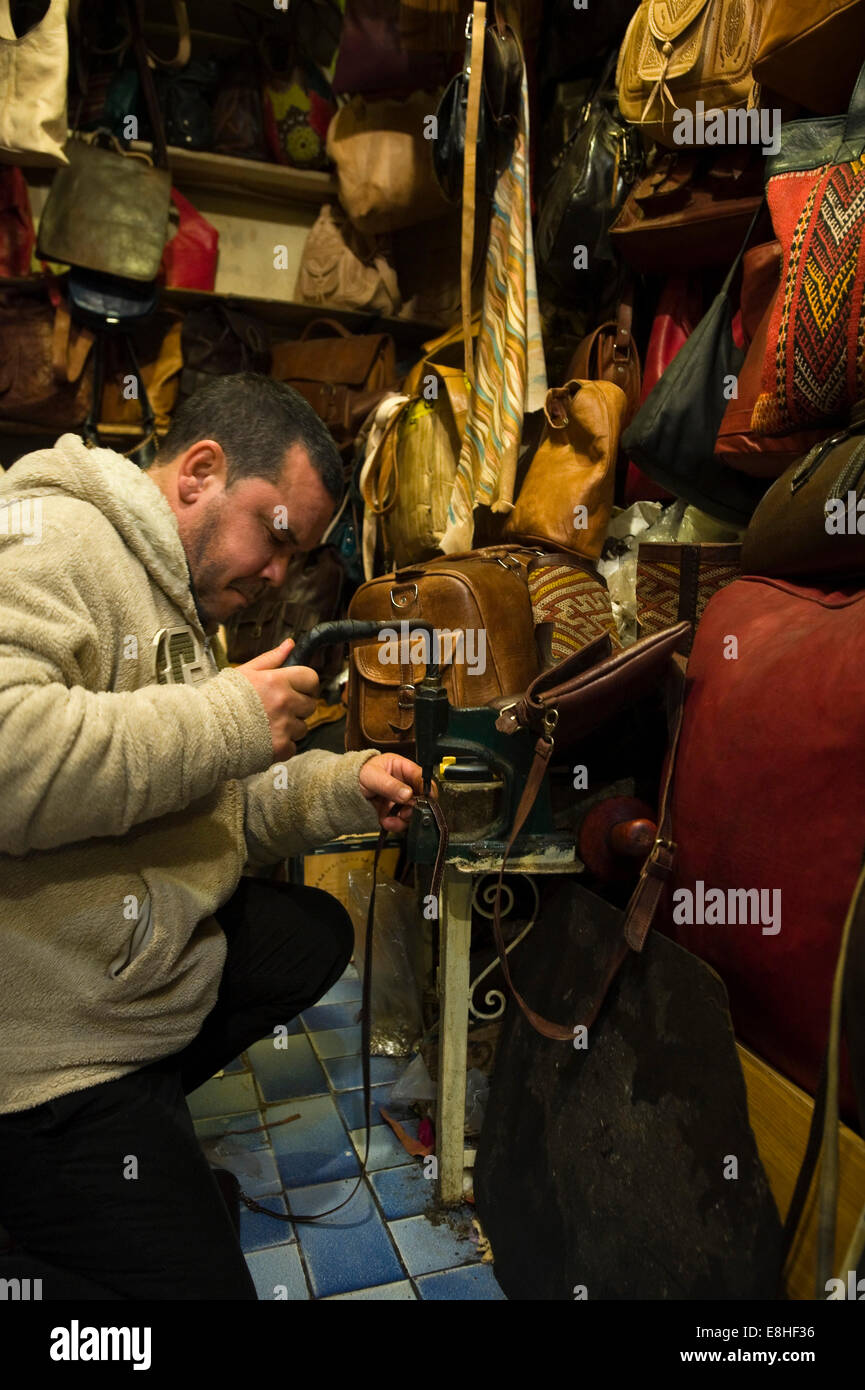 Ritratto verticale di un leatherworker fori di punzonatura in un cinturino in pelle di un negozio nel souk di Marrakech. Foto Stock