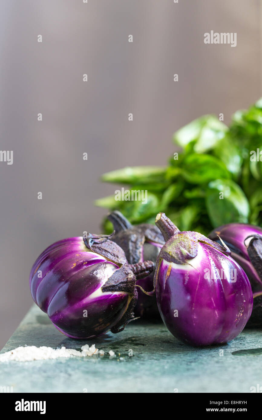 Gruppo di melanzane su marmo verde, con sale di primo piano e di basilico in background. Foto Stock