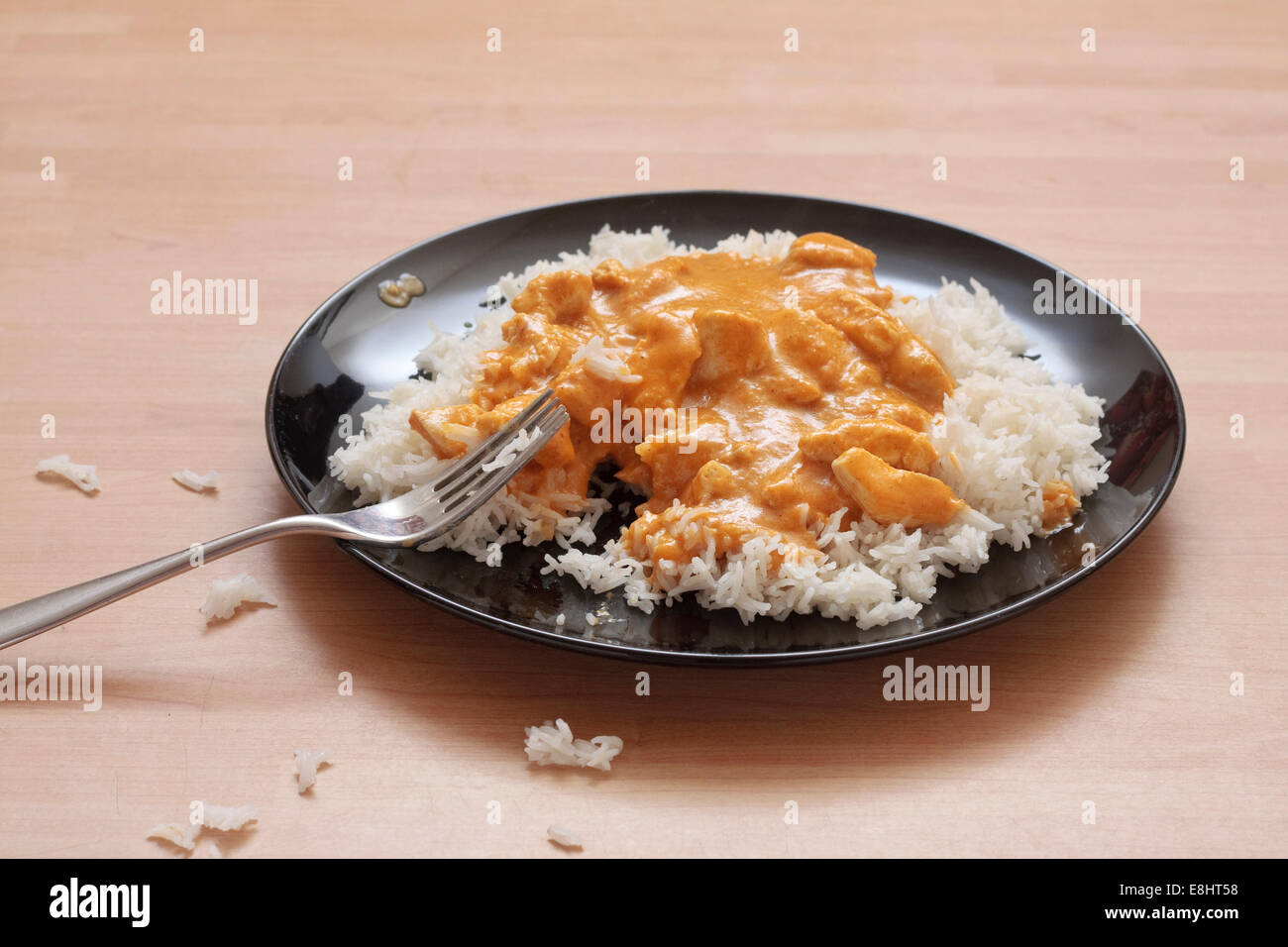Una piastra di korma di pollo e riso su una piastra nera con riso interrotte intorno a piastra sulla tabella Foto Stock