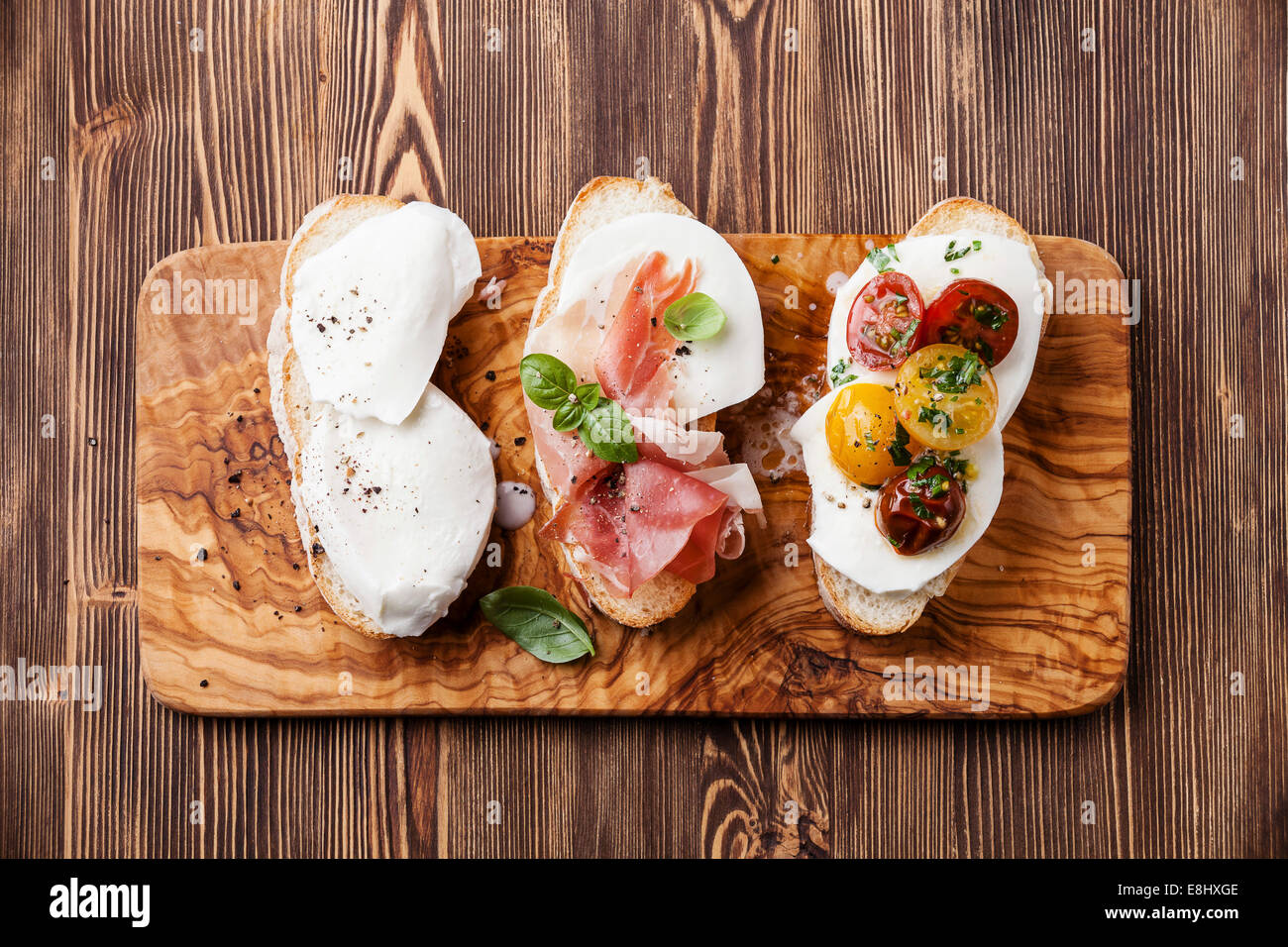 Tre bruschette con mozzarella prosciutto e pomodori arrostiti sulla ciabatta pane su sfondo di legno Foto Stock