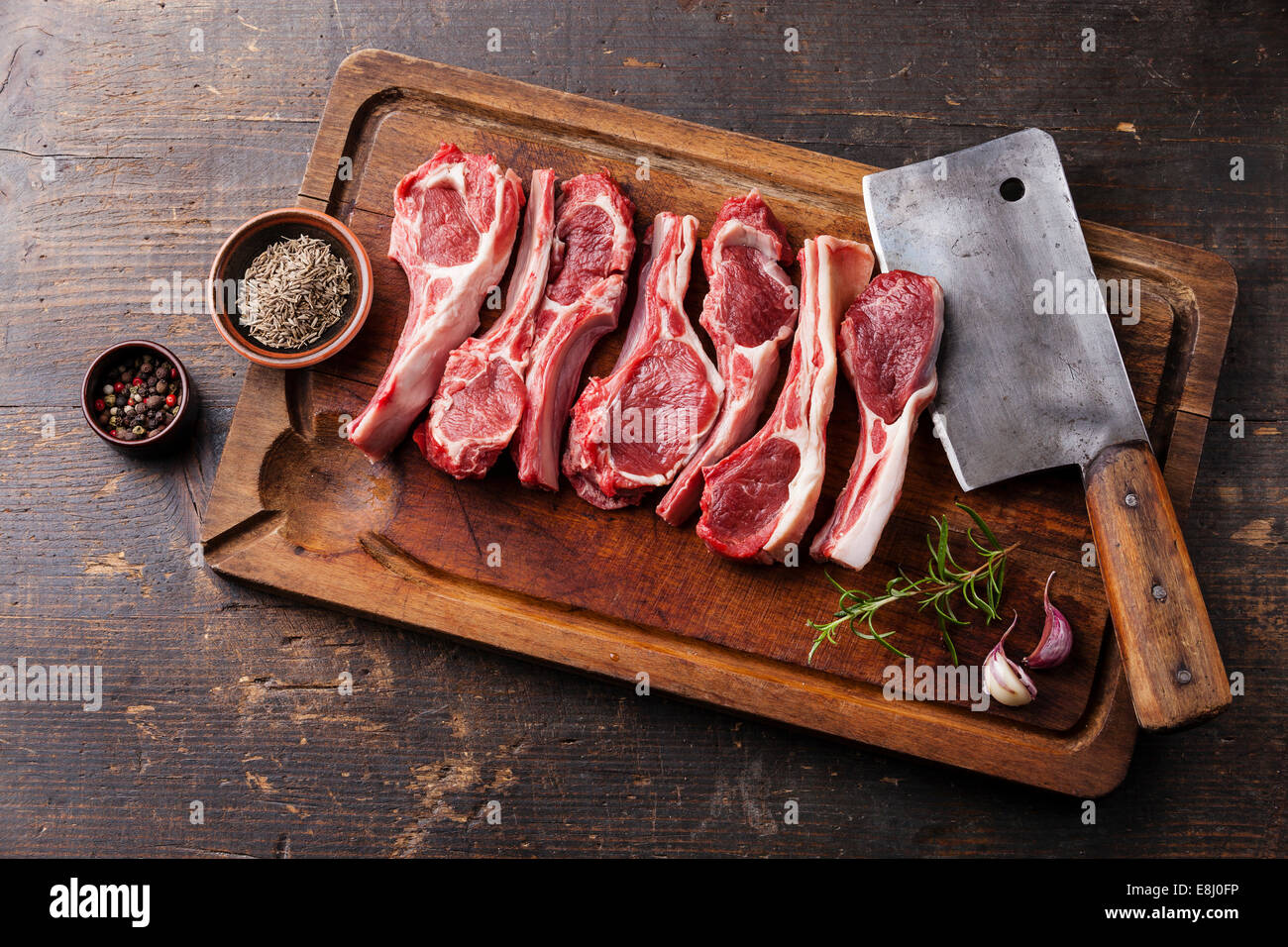 Crudo fresco costolette d'agnello con pepe e cumino e carne cleaver sul tagliere di legno su sfondo scuro Foto Stock