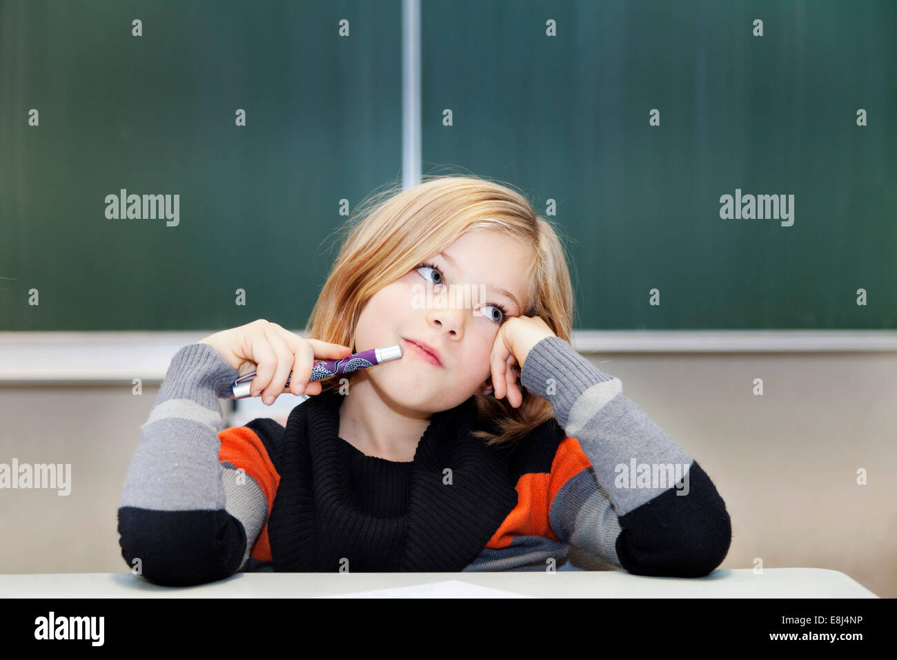 La scolaretta, 9 anni, pensieroso, seduto di fronte a una lavagna Foto Stock
