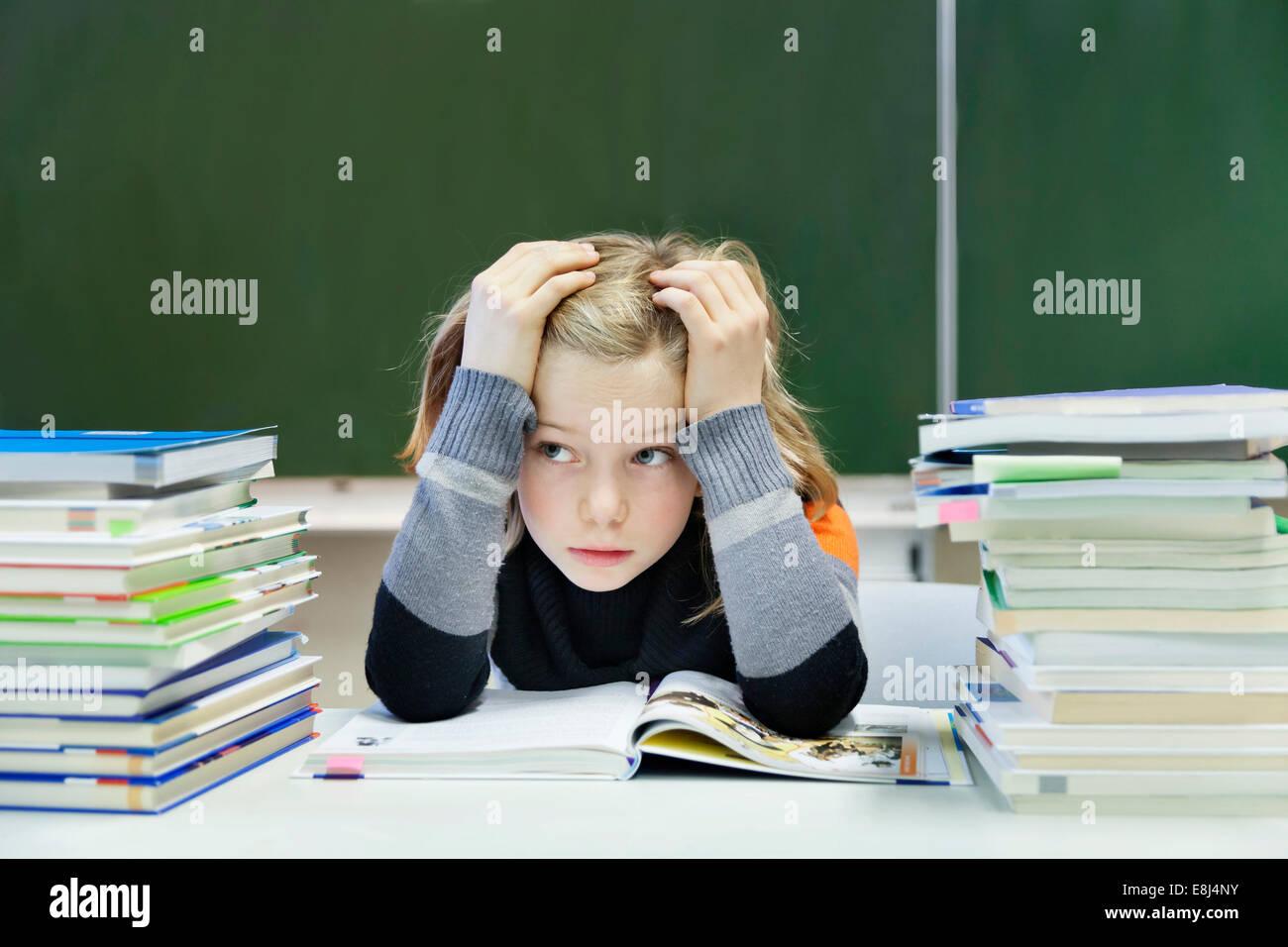 Oberati da studentessa, 9 anni, seduta con due pile di libri di fronte a una lavagna Foto Stock