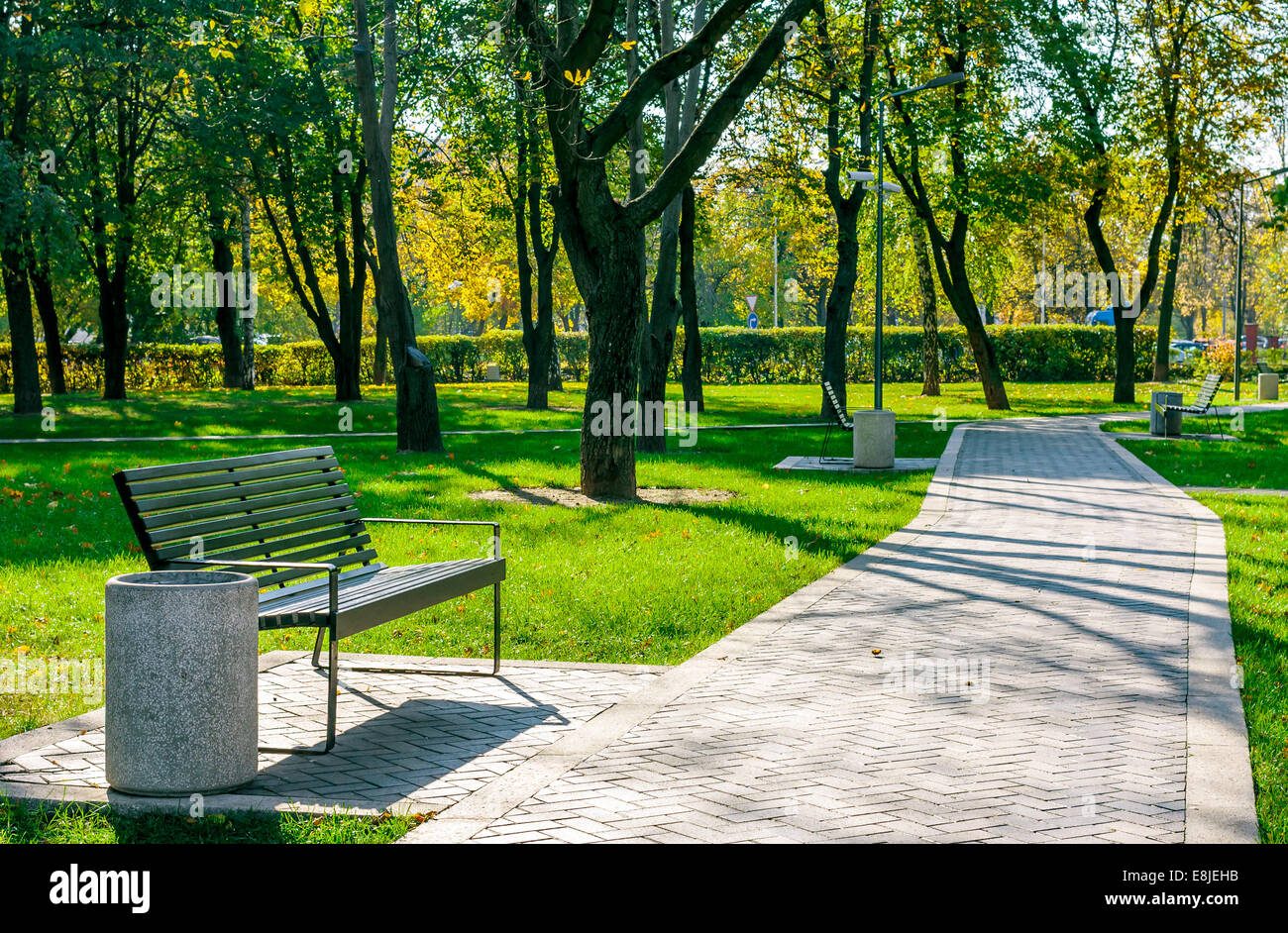 Panca vicino al percorso del cemento in un tranquillo parco della città inizio autunno in una giornata di sole Foto Stock