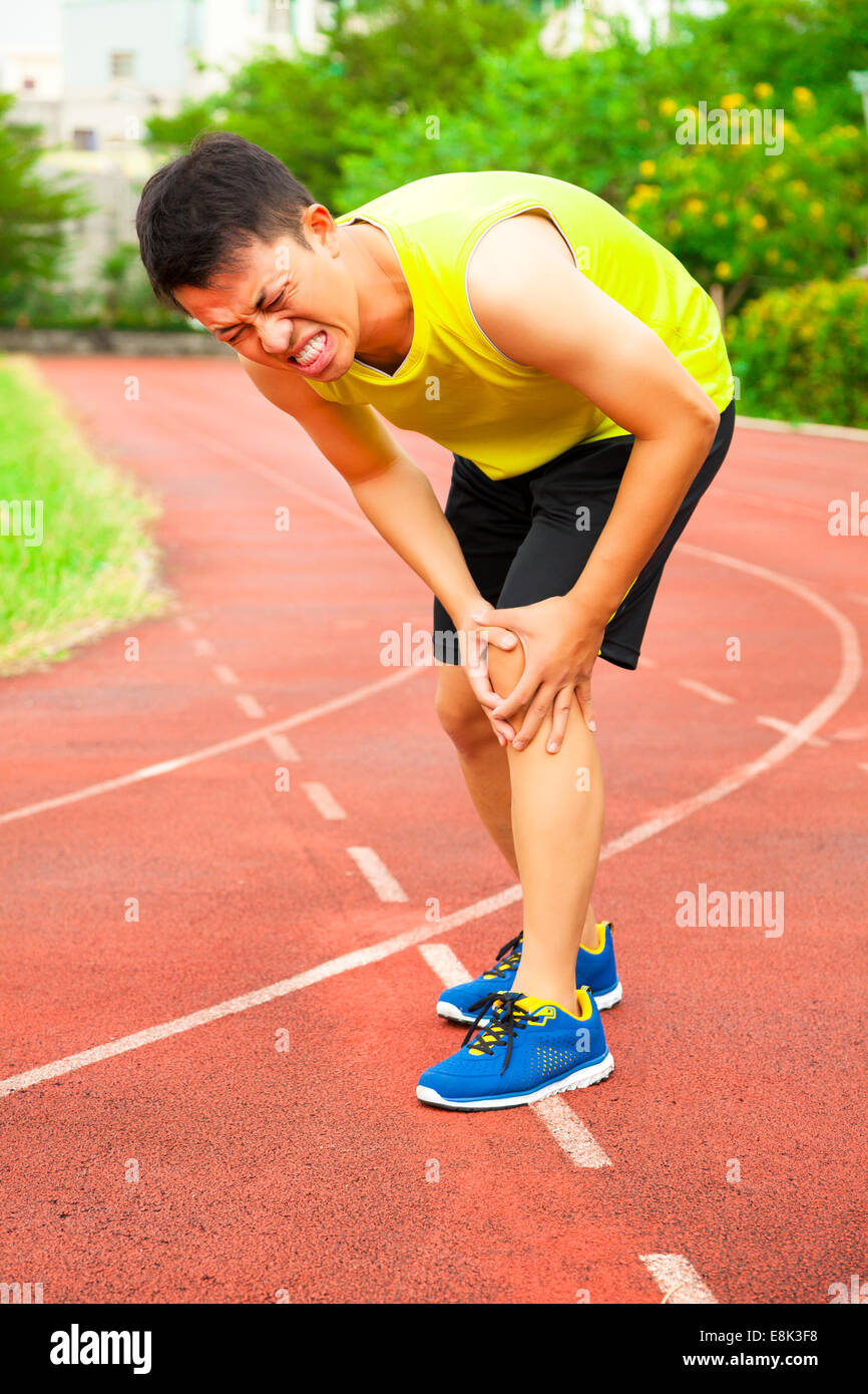 Giovane maschio runner che soffrono di lesioni del ginocchio sulla pista dello stadio Foto Stock