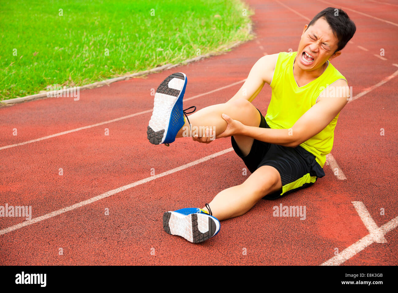 Giovane maschio runner che soffrono di crampo alla gamba sulla pista dello stadio Foto Stock