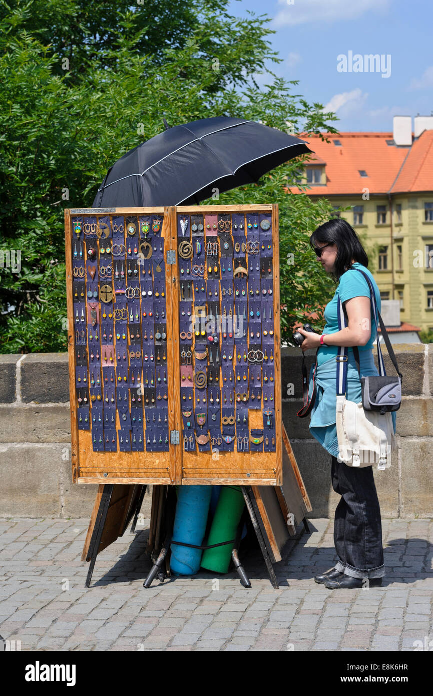 Una donna da parte di un piccolo box signore di vendita gioielli fatti a mano sul Ponte Carlo a Praga Repubblica Ceca. Foto Stock