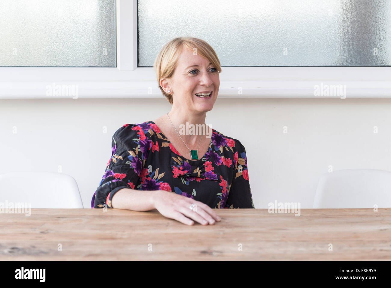 Una donna con capelli corti si siede a un tavolo di legno sorridente. Cucina / sala riunioni. Business donna / madre Foto Stock