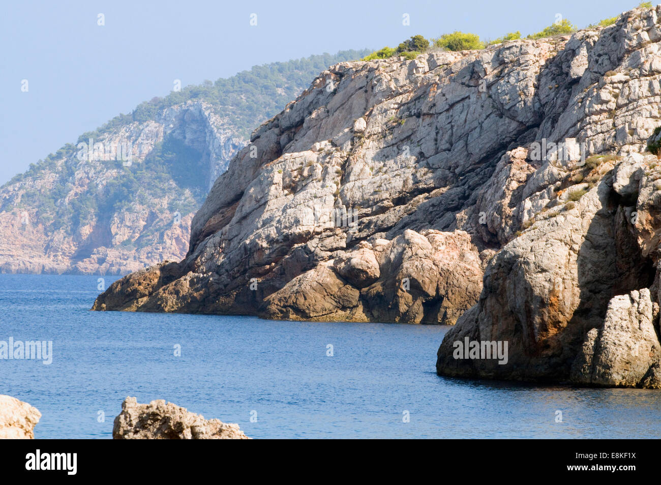 Isola rocciosa costa sulla tranquilla blu Mare Mediterraneo con il promontorio boscoso in background Foto Stock