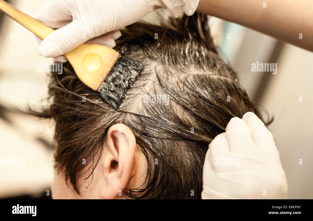 Giovane donna caucasica al servizio parrucchiere mettendo il colore con le mani sui capelli bagnati, back shot close up Foto Stock