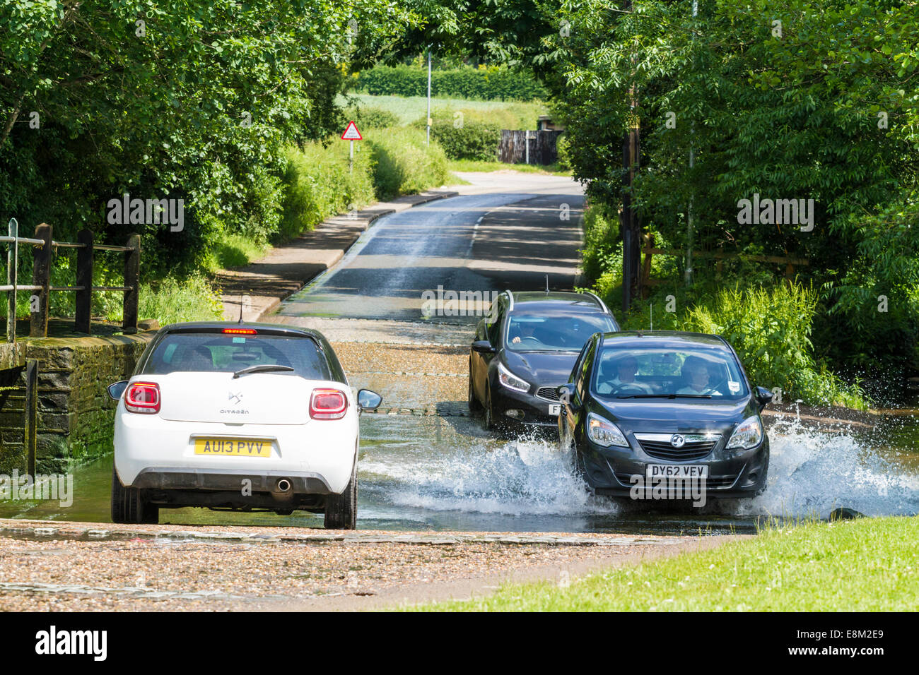 Cars driving attraverso un flusso. Auto in attesa di attraversare una ford come altri drive attraverso l'acqua e la strada di Rufford, Nottinghamshire, England, Regno Unito Foto Stock