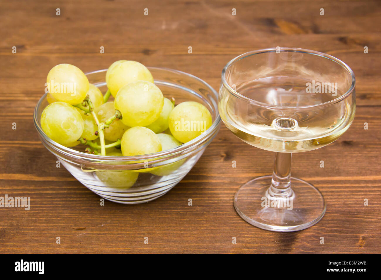 Un bicchiere di vino e di uve in una ciotola sul tavolo di legno Foto Stock