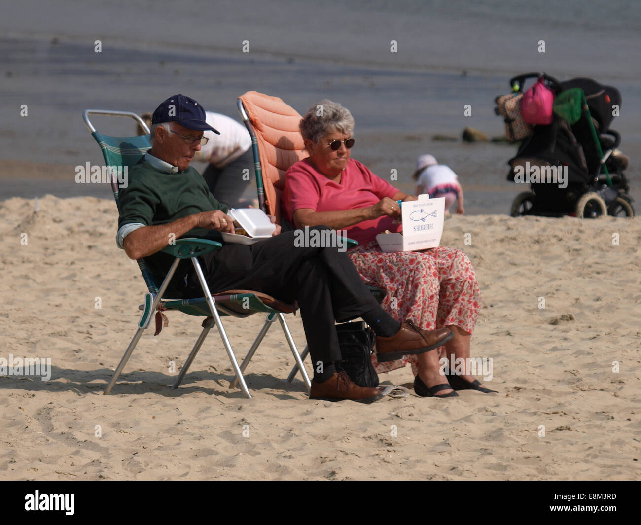 I pensionati a mangiare pesce e patatine sulla spiaggia a Lyme Regis, Dorset, Regno Unito Foto Stock