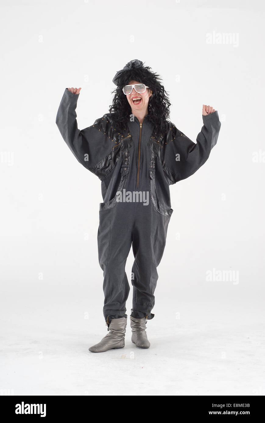 Donna in costume costume della commedia in uno degli anni ottanta, moda vestito con larghi nero tutina, grande parrucca, argento stivali & white glas Foto Stock