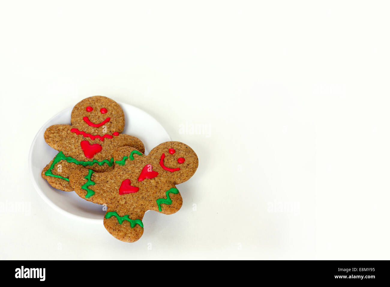 Un Natale di Gingerbread Man cookie con cuori sulla sua maglietta si posa su una piastra bianca con una donna di panpepato, su un bianco isol Foto Stock