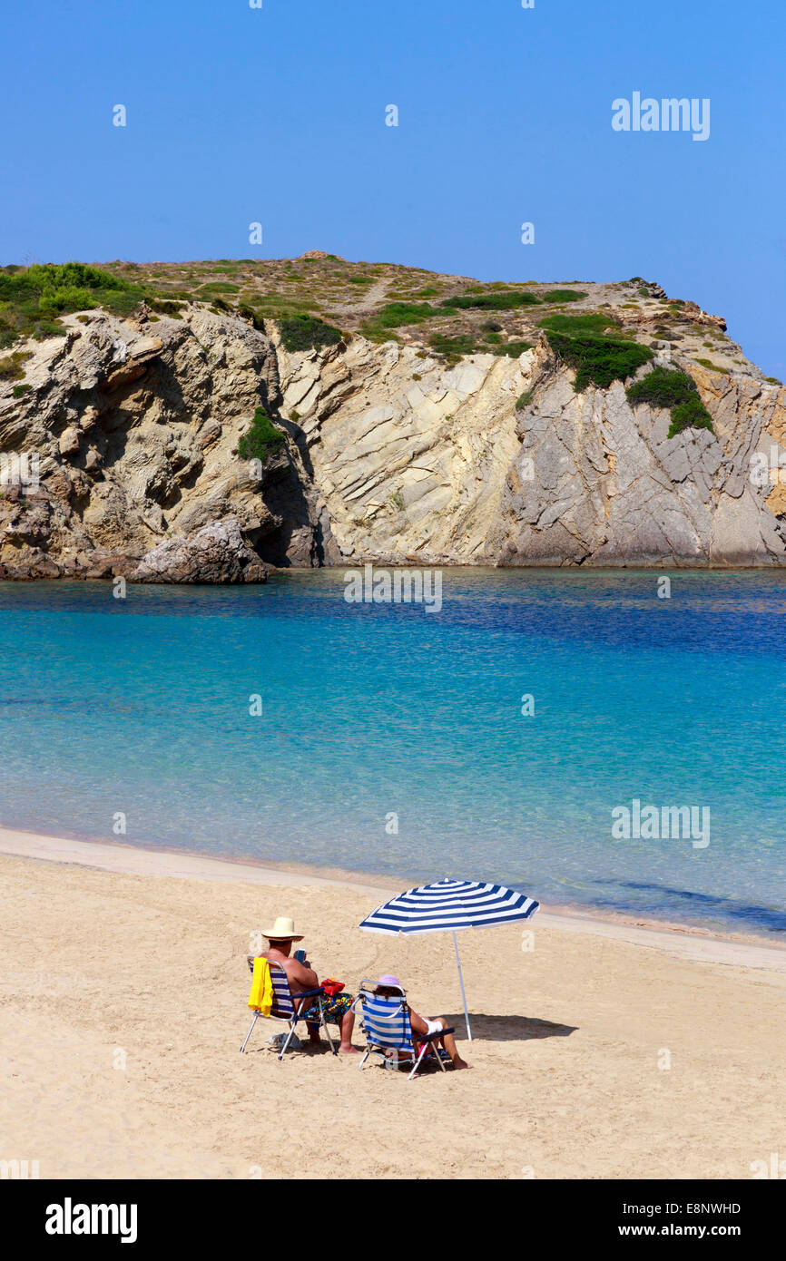Uomo che indossa due cappelli, e una donna seduta sulla sdraio con un ombrellone sulla spiaggia in Arenel d'en Castell, Menorca, Foto Stock