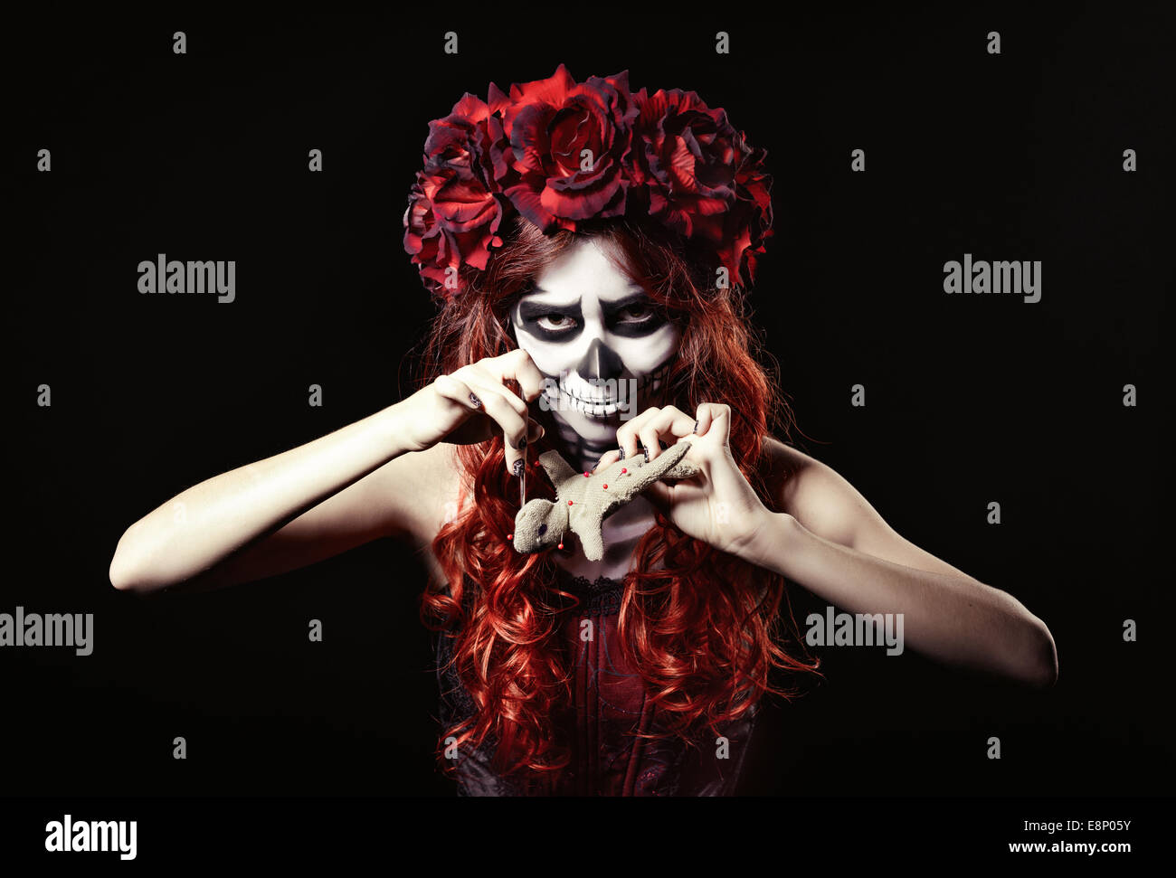 Giovane strega voodoo con trucco muertos (zucchero cranio) perforare una bambola Foto Stock