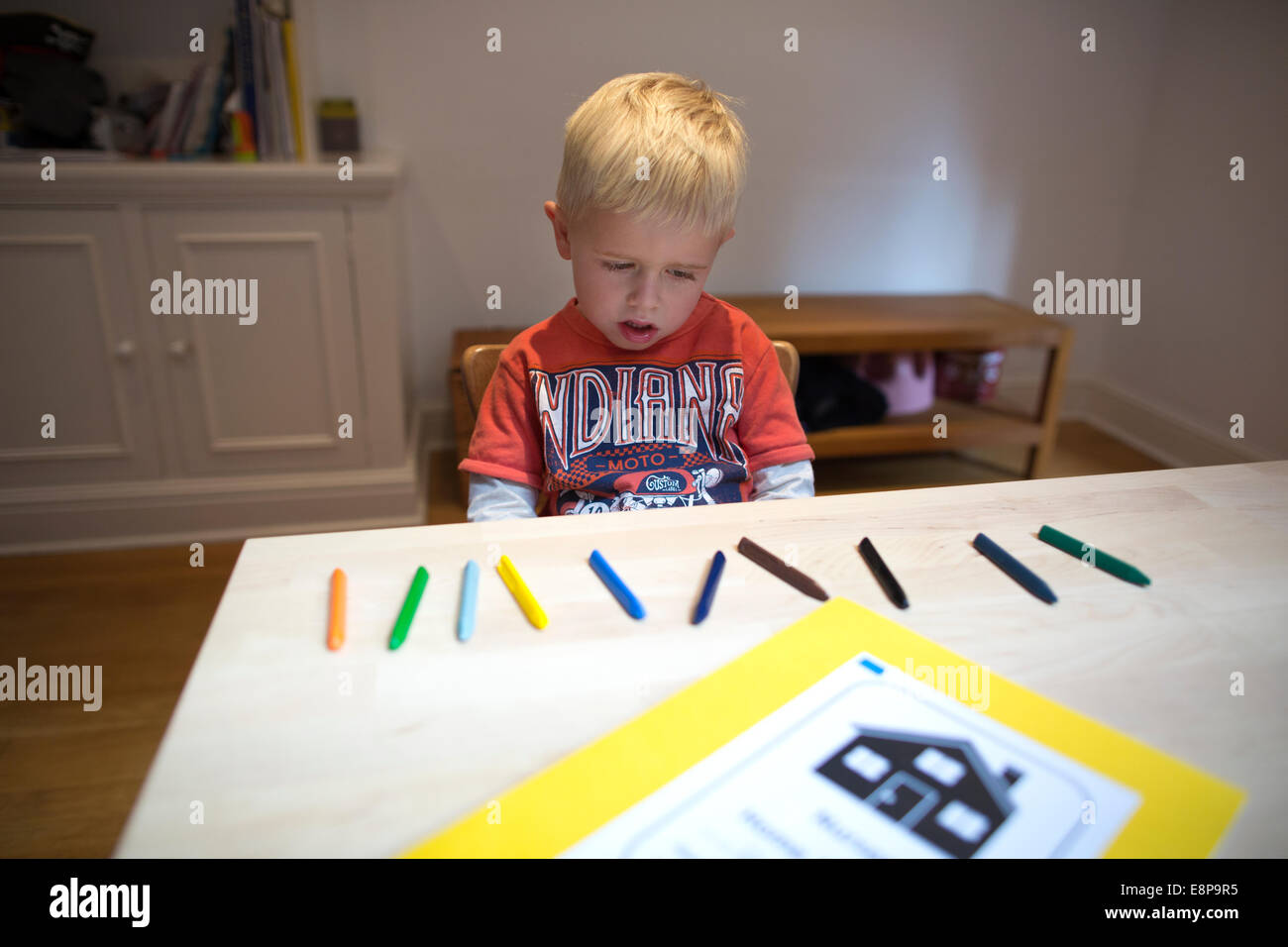 4 anno vecchio ragazzo si siede a un tavolo a casa con i bambini di pastelli come parte di un esercizio di conteggio per la sua scuola materna di compiti Foto Stock