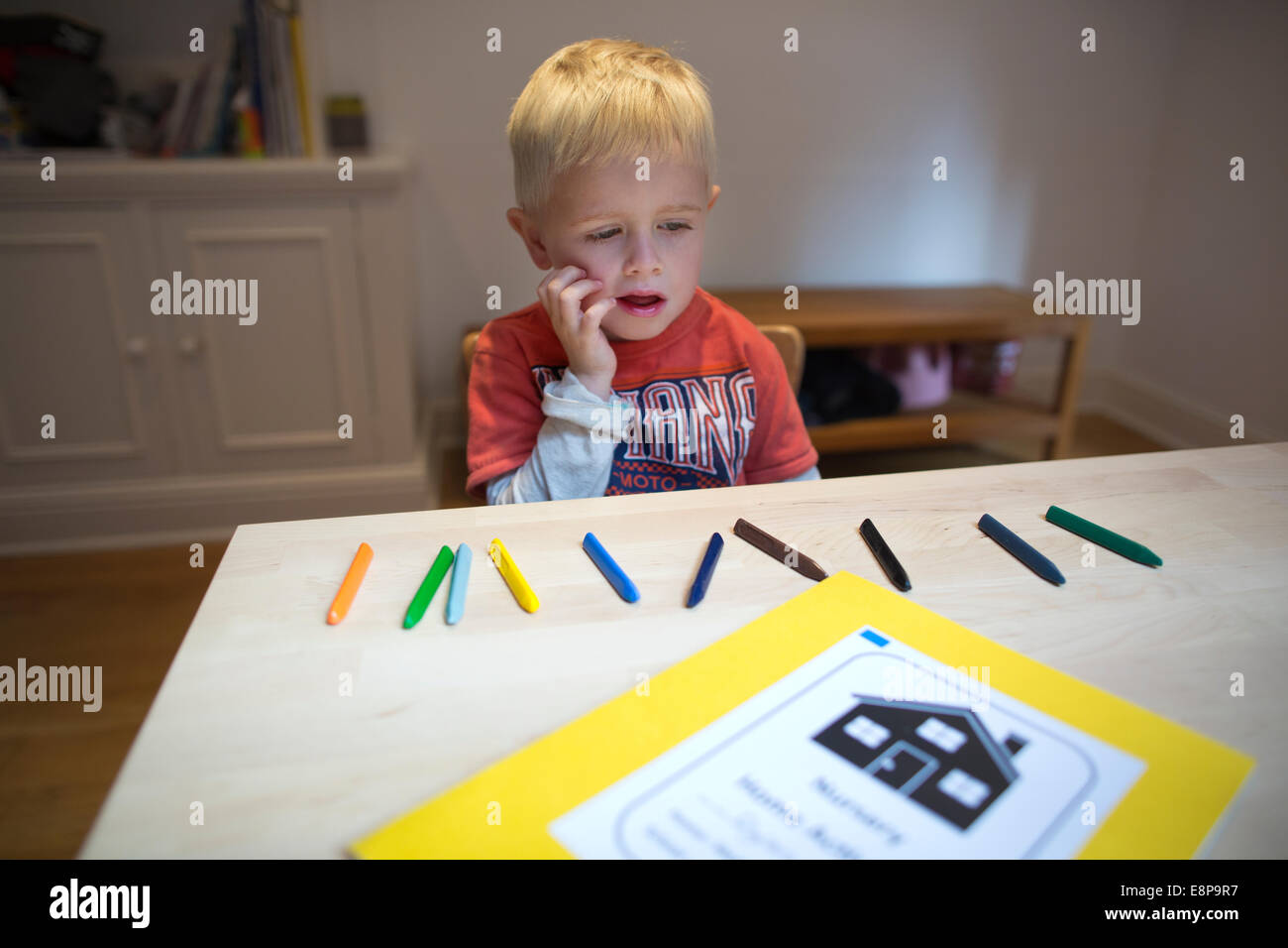 4 anno vecchio ragazzo si siede a un tavolo a casa con i bambini di pastelli come parte di un esercizio di conteggio per la sua scuola materna di compiti Foto Stock
