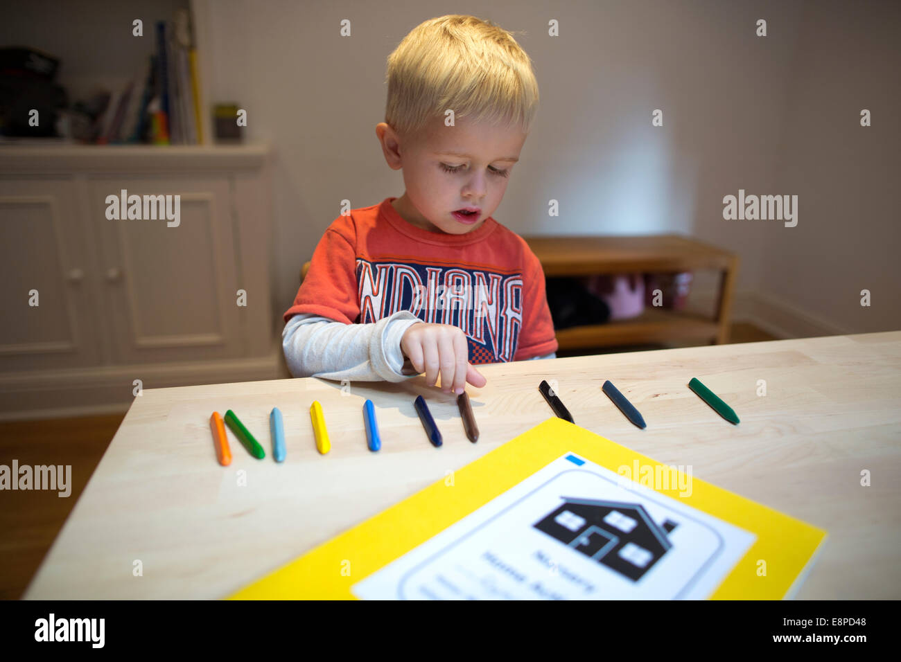 4 anno vecchio ragazzo si siede a un tavolo a casa con i bambini di pastelli come parte di un esercizio di conteggio per la sua scuola materna di compiti Foto Stock
