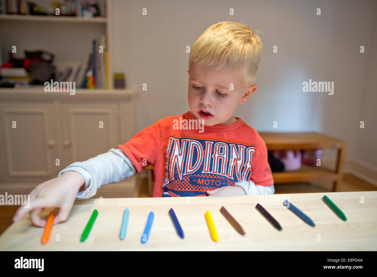 4 anno vecchio ragazzo si siede a un tavolo a casa con i bambini di pastelli come parte di un esercizio di conteggio per la sua scuola materna di compiti Foto Stock