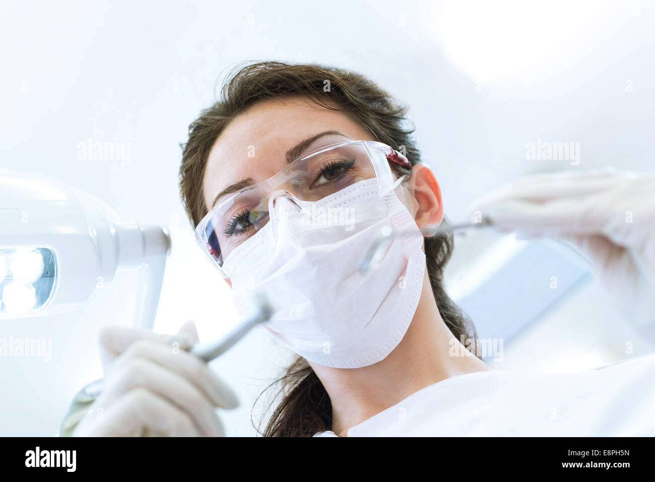 Dentista indossando maschera chirurgica tenendo angolato e specchio del trapano, pronto per iniziare Foto Stock