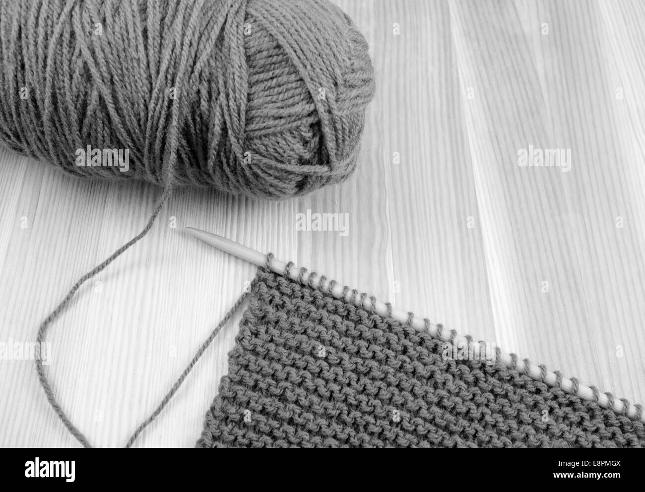 Chiusura del gomitolo di lana con lunghezza di garter stitch su un ago di lavorazione a maglia, su legno - elaborazione monocromatica Foto Stock