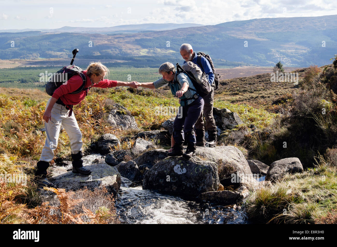 Una donna escursionista escursionismo aiutando qualcuno che attraversa un ruscello di montagna su pendii di Moel Siabod nel Parco Nazionale di Snowdonia North Wales UK Foto Stock