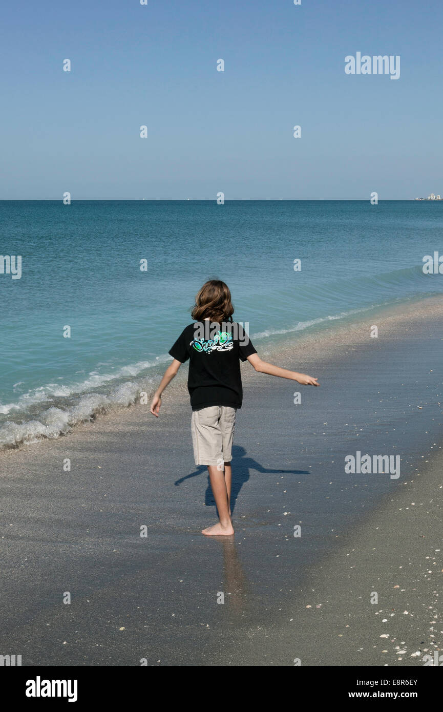 Lungo capelli presteen ragazzo a piedi da solo sulla spiaggia saltando pietre, Turtle Beach, Sarasota County, Florida Foto Stock