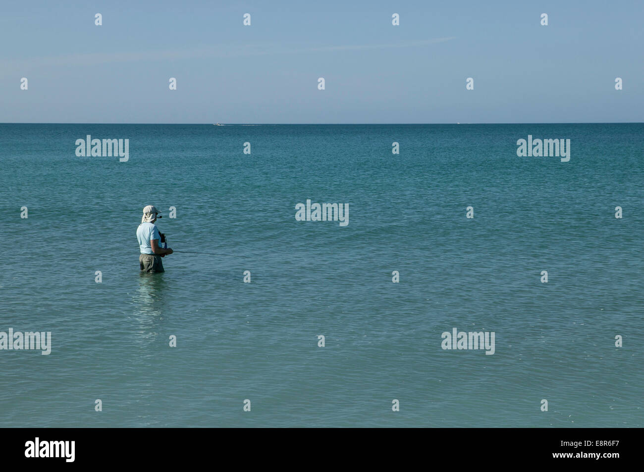 Pescatore solitario che fuma un tubo e coscia in piedi in profondità in acqua sulla costa del Golfo della Florida, Sarasota, Florida. Foto Stock