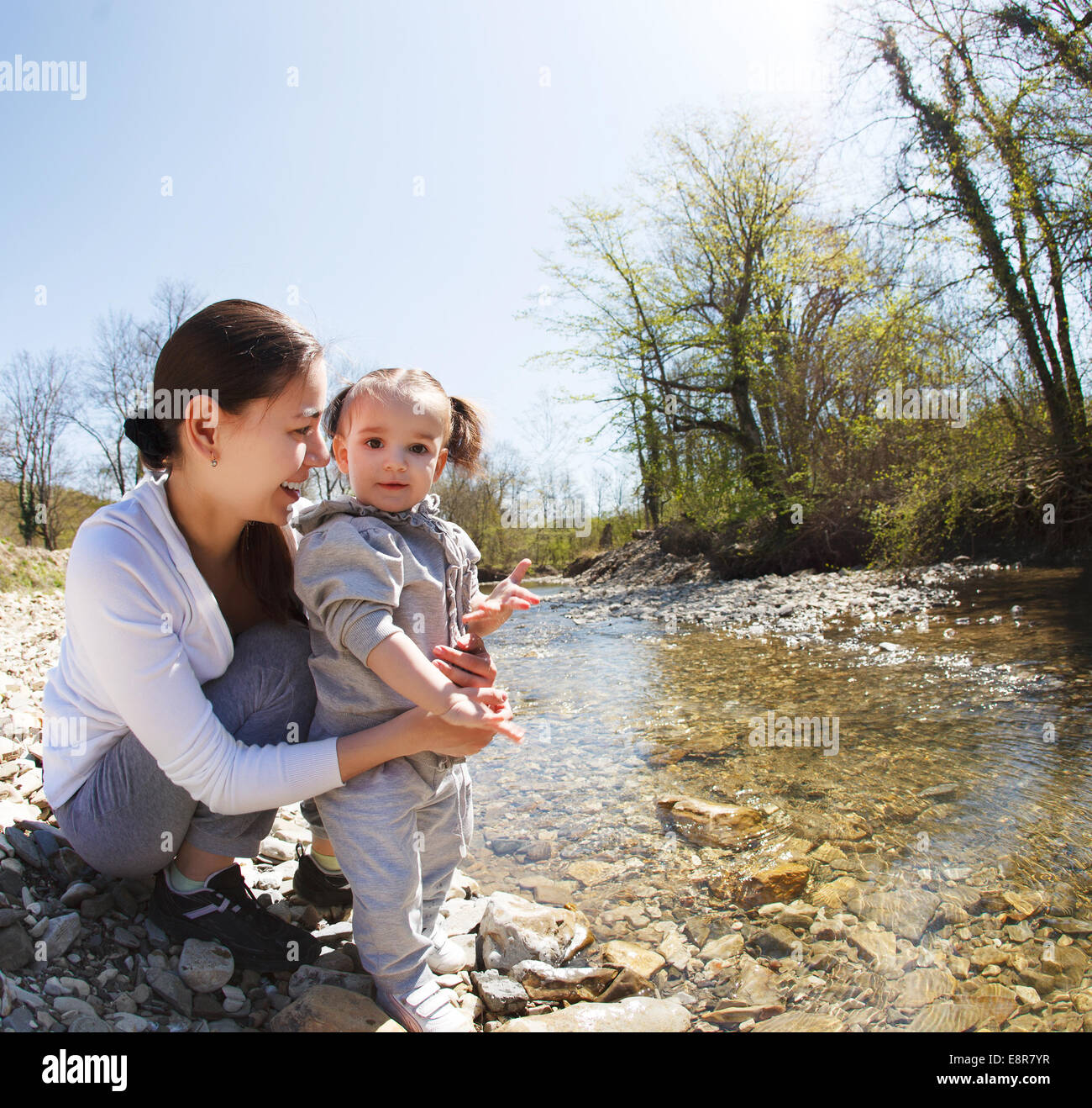 Felice giovane madre con figlia piccola vicino al fiume di montagna all'aperto Foto Stock