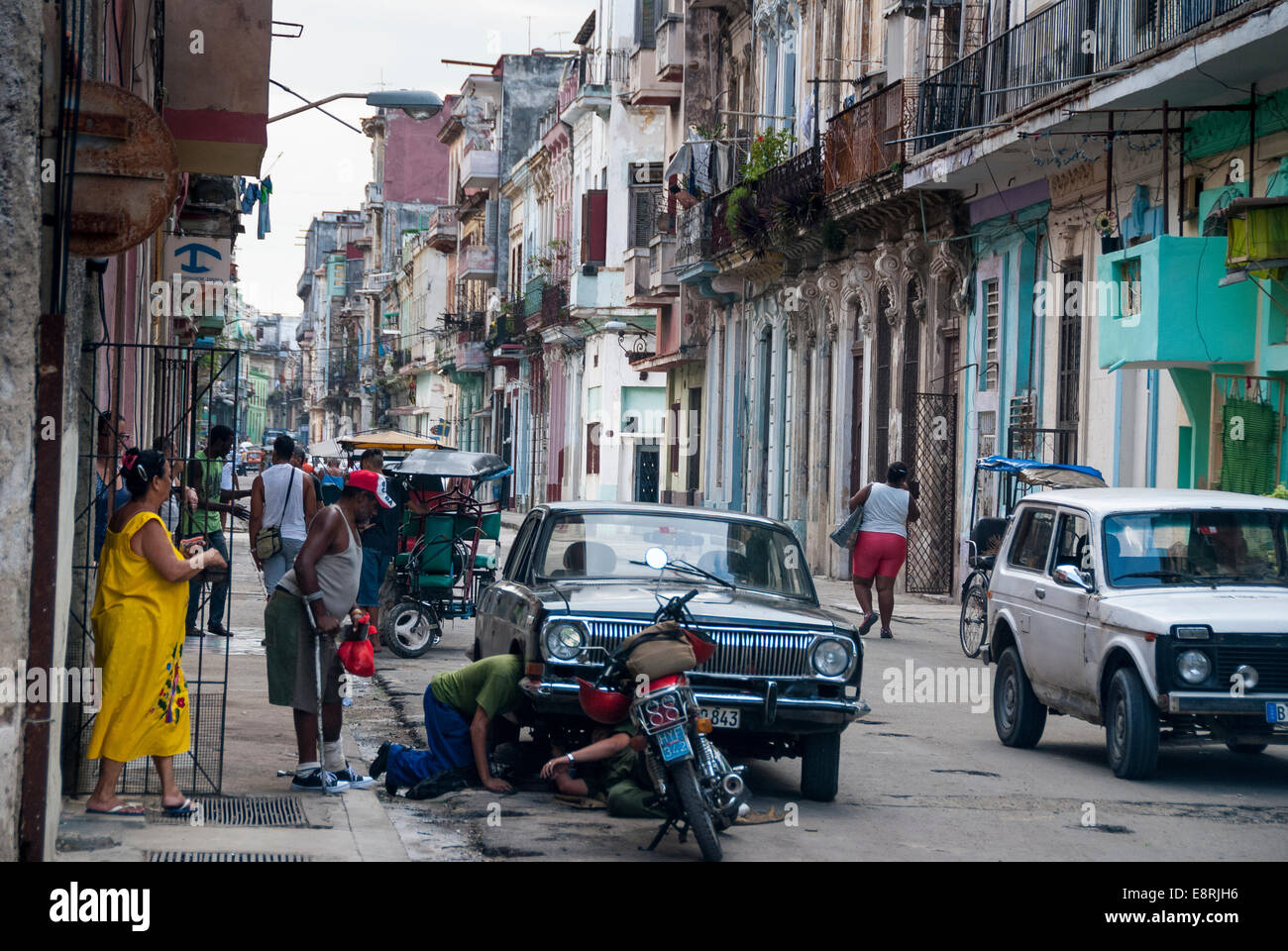 Havana Cuba - curiosi guarda come due uomini cercano di fare le riparazioni improvvisate su un vintage americano auto in un Central Havana street. Foto Stock
