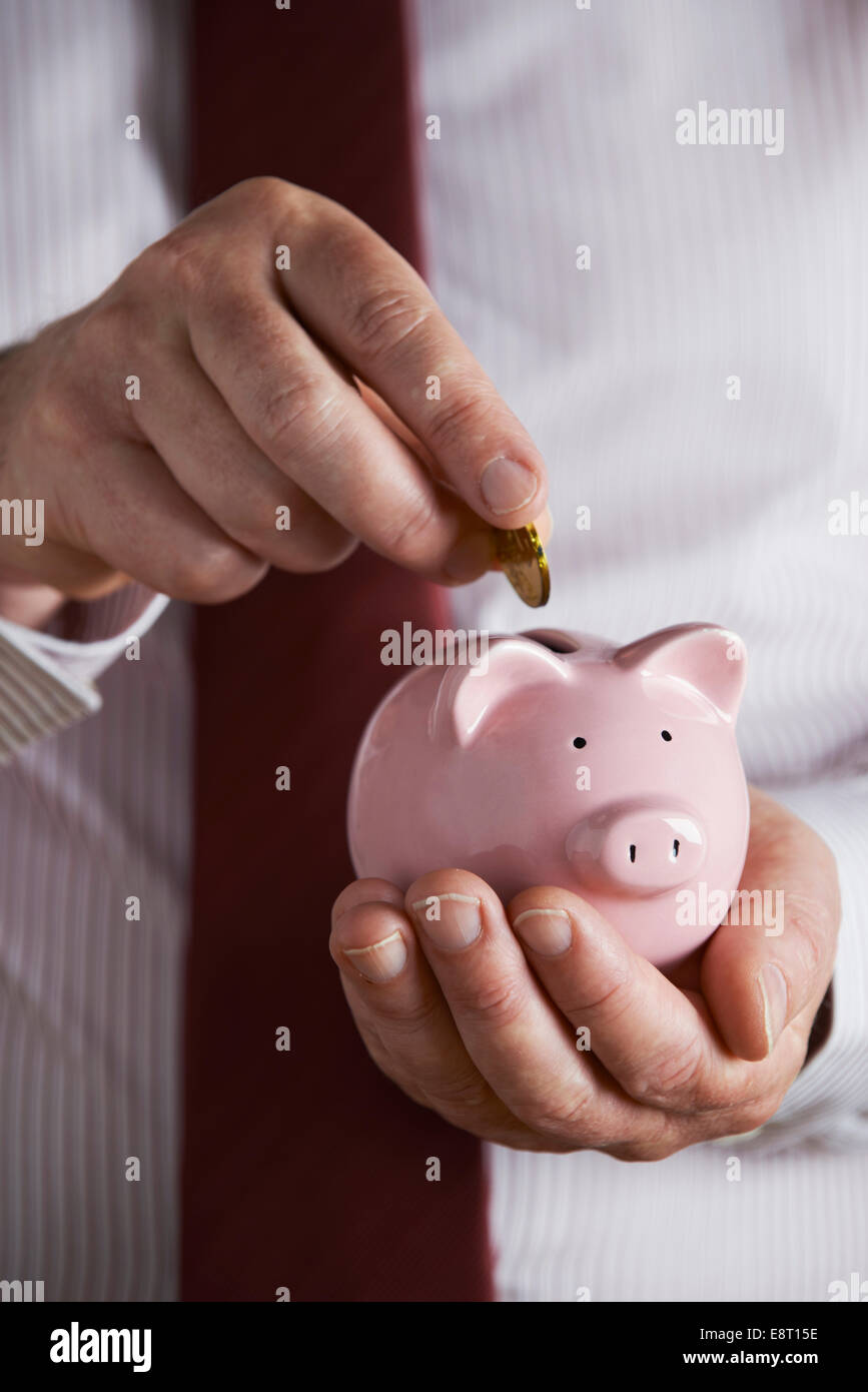 Imprenditore mettendo moneta nel salvadanaio Foto Stock