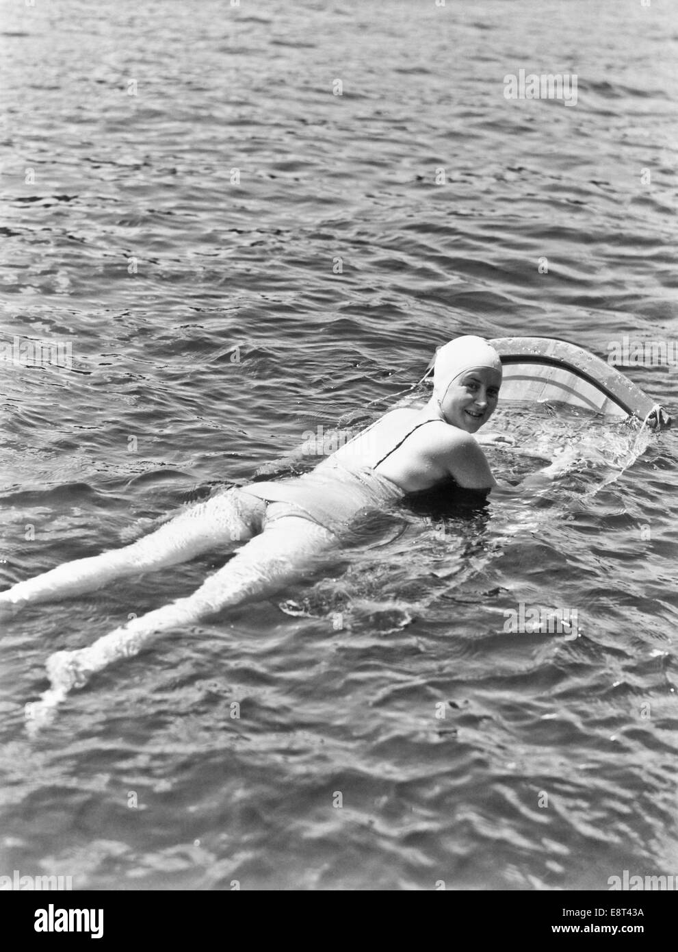 1930s 1940s donna indossare CUFFIA DA BAGNO UN PEZZO SUIT giacente su AQUA SKI BOARD guardare fotocamera sulla spalla lago Muskoka in Canada Foto Stock