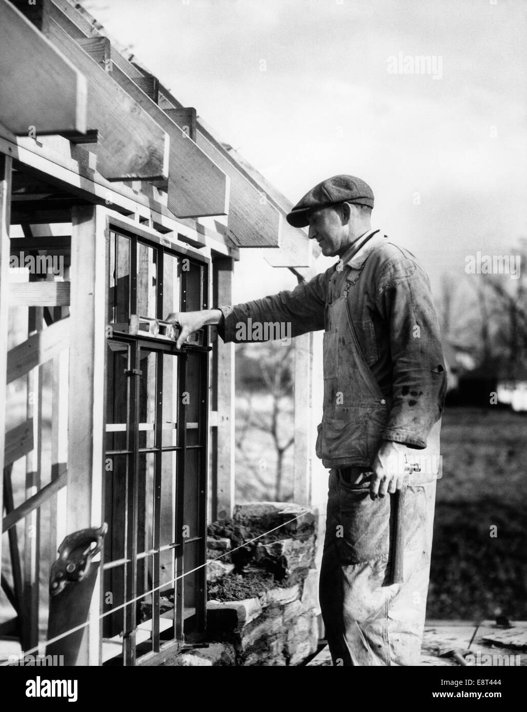 1930s uomo CARPENTER AL SITO IN COSTRUZIONE IN LEGNO edificio incorniciato tenendo premuto Controllo del livello di installare sul telaio di una finestra Foto Stock