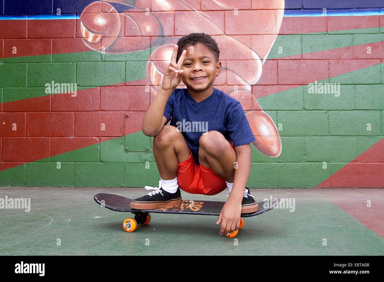 African American boy seduto su skateboard da urban murale Foto Stock