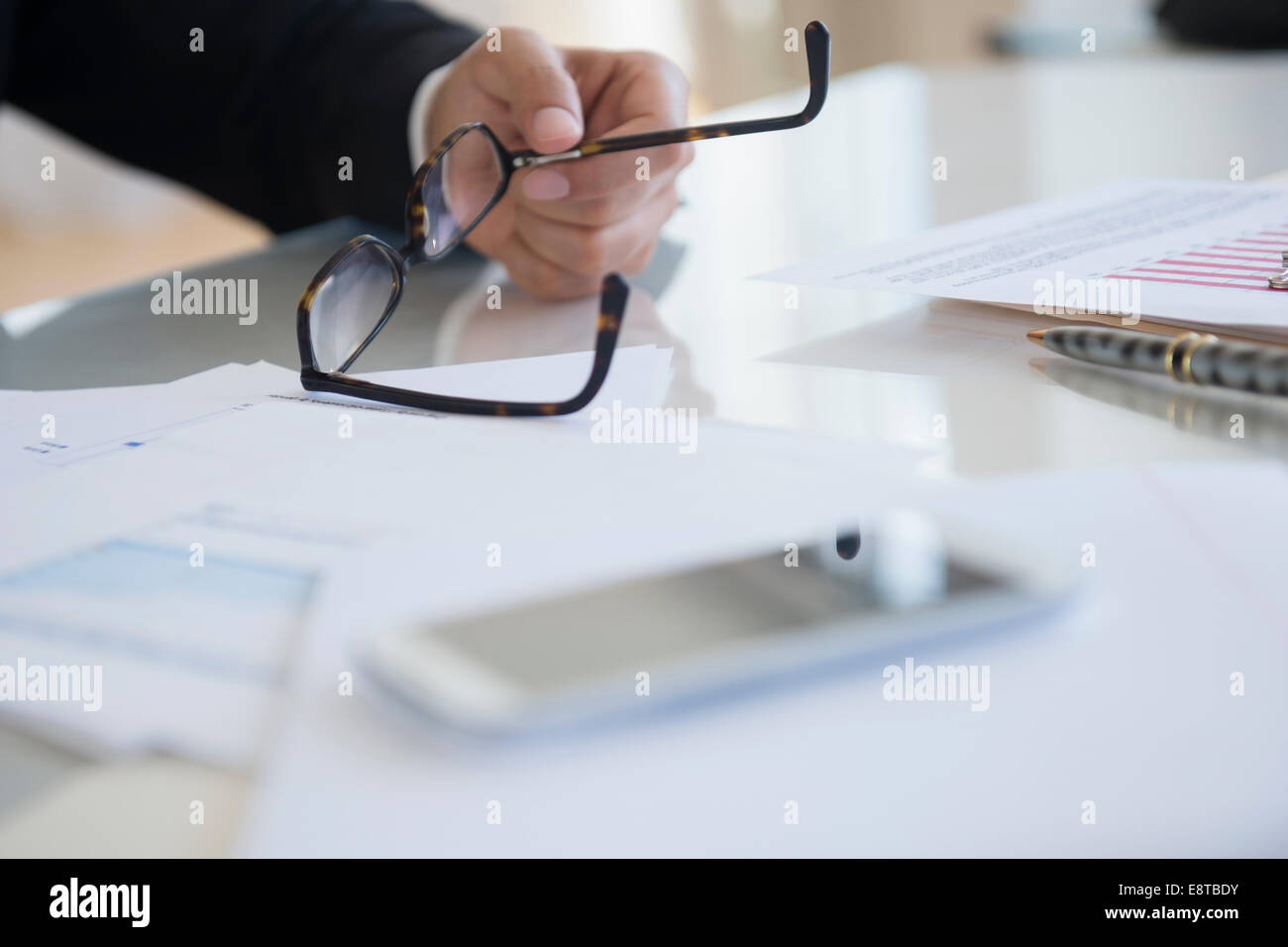 Close up di razza mista imprenditore tenendo occhiali alla scrivania Foto Stock