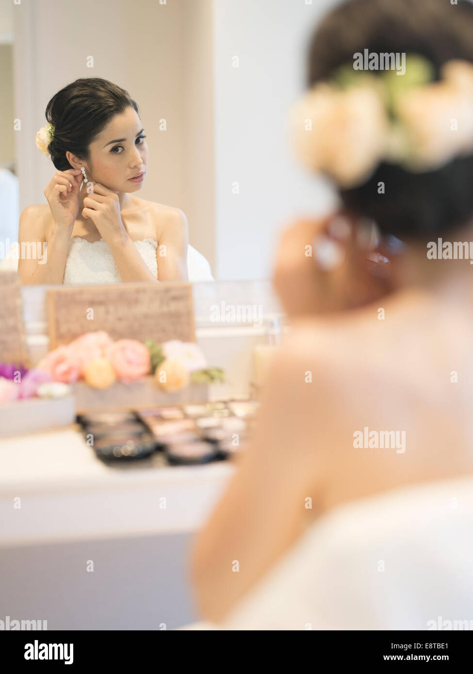 Razza mista, Asian / American sposa in bianco abito da sposa mette il trucco e orecchini prima del matrimonio Foto Stock