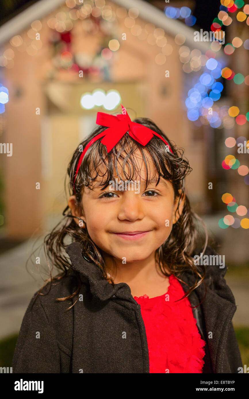 Ispanico ragazza sorridente al di fuori di casa decorata con luci di stringa Foto Stock