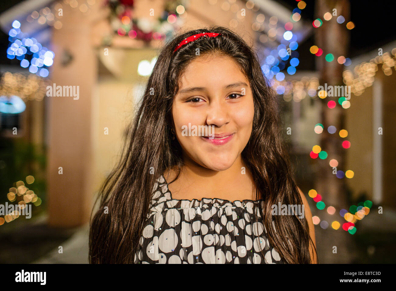 Ispanico ragazza sorridente al di fuori di casa decorata con luci di stringa Foto Stock