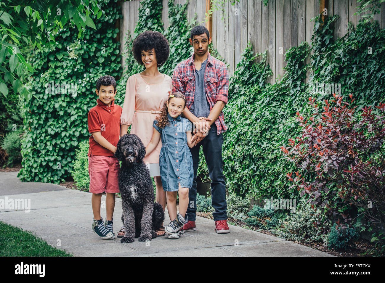 Razza mista madre e bambini sorridenti con il cane sul marciapiede suburbana Foto Stock