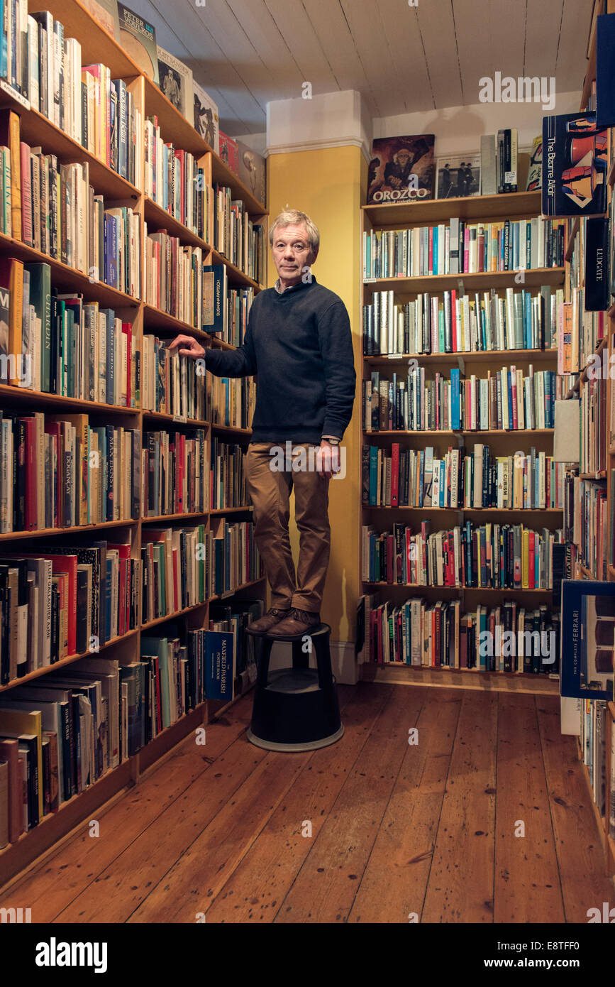 Un ritratto di un libraio che vende di seconda mano libri nel suo negozio con i libri disposti ordinatamente su scaffali come una libreria Foto Stock