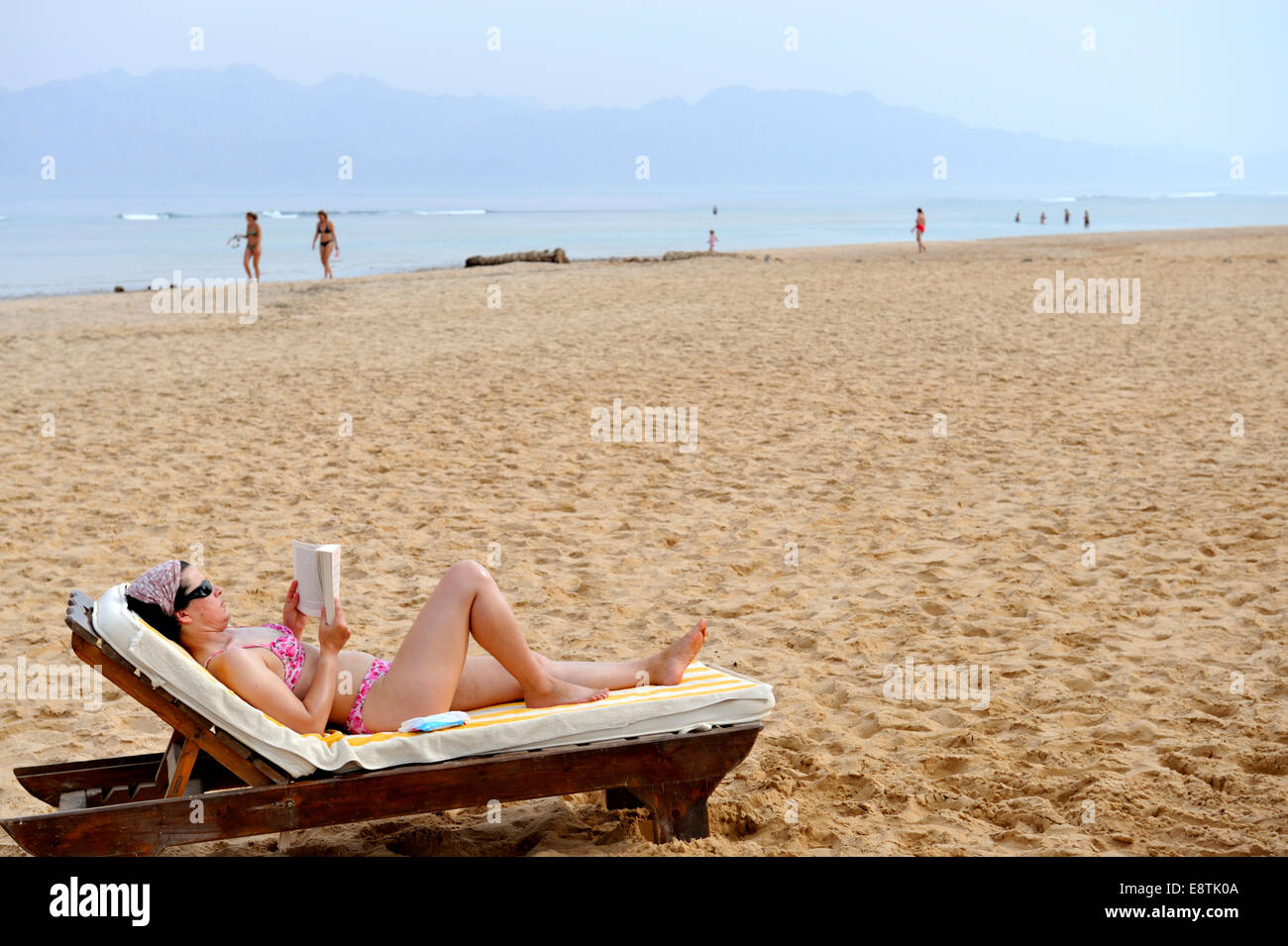 La donna a prendere il sole sulla spiaggia con libro Foto Stock