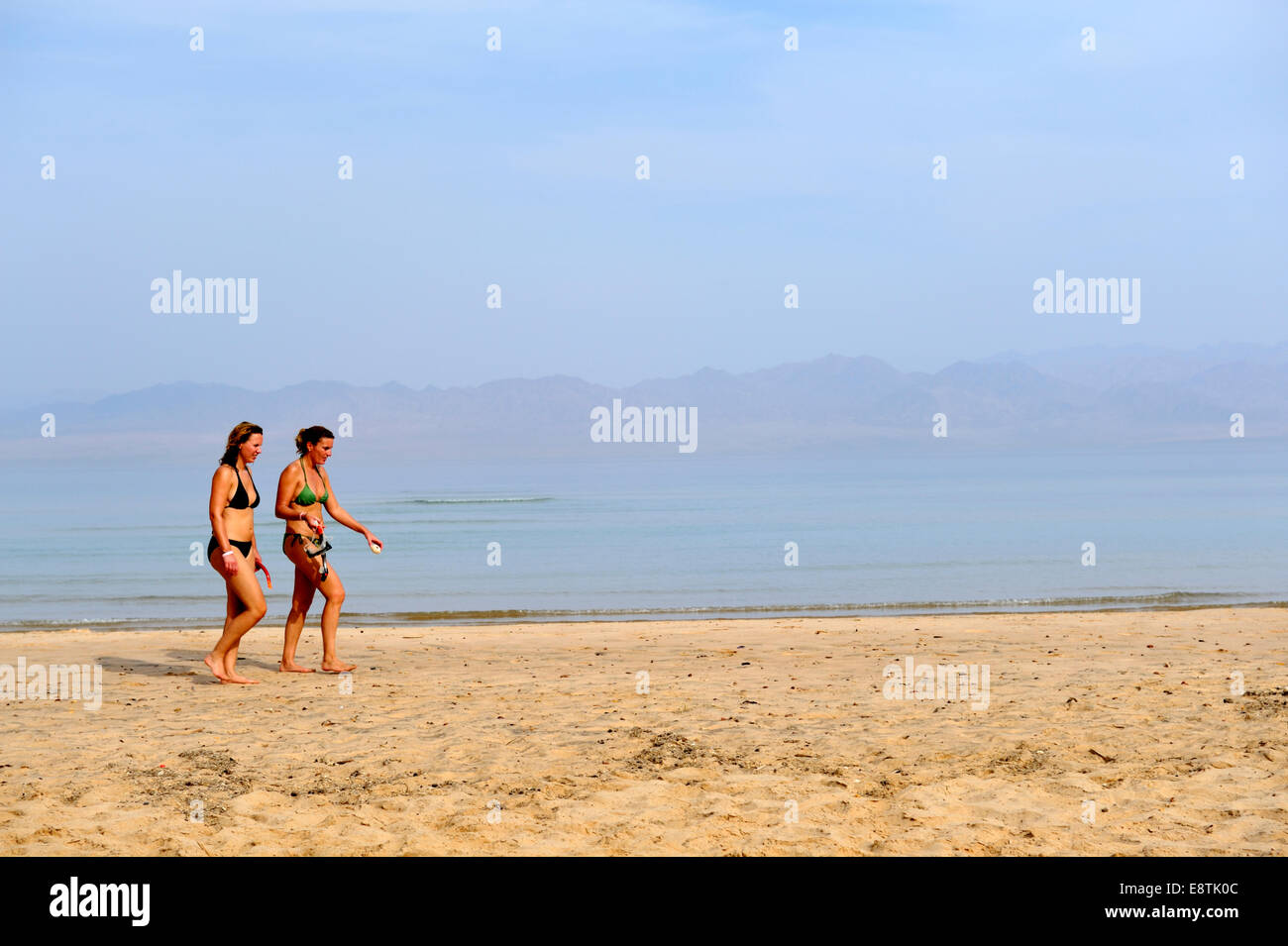 Due donne a piedi lungo la spiaggia di sabbia in riva al mare a Foto Stock
