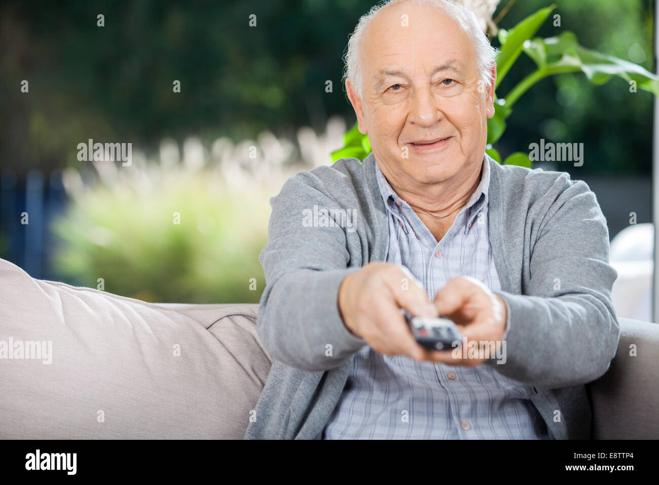 Uomo anziano utilizzando il telecomando mentre è seduto sul lettino Foto Stock
