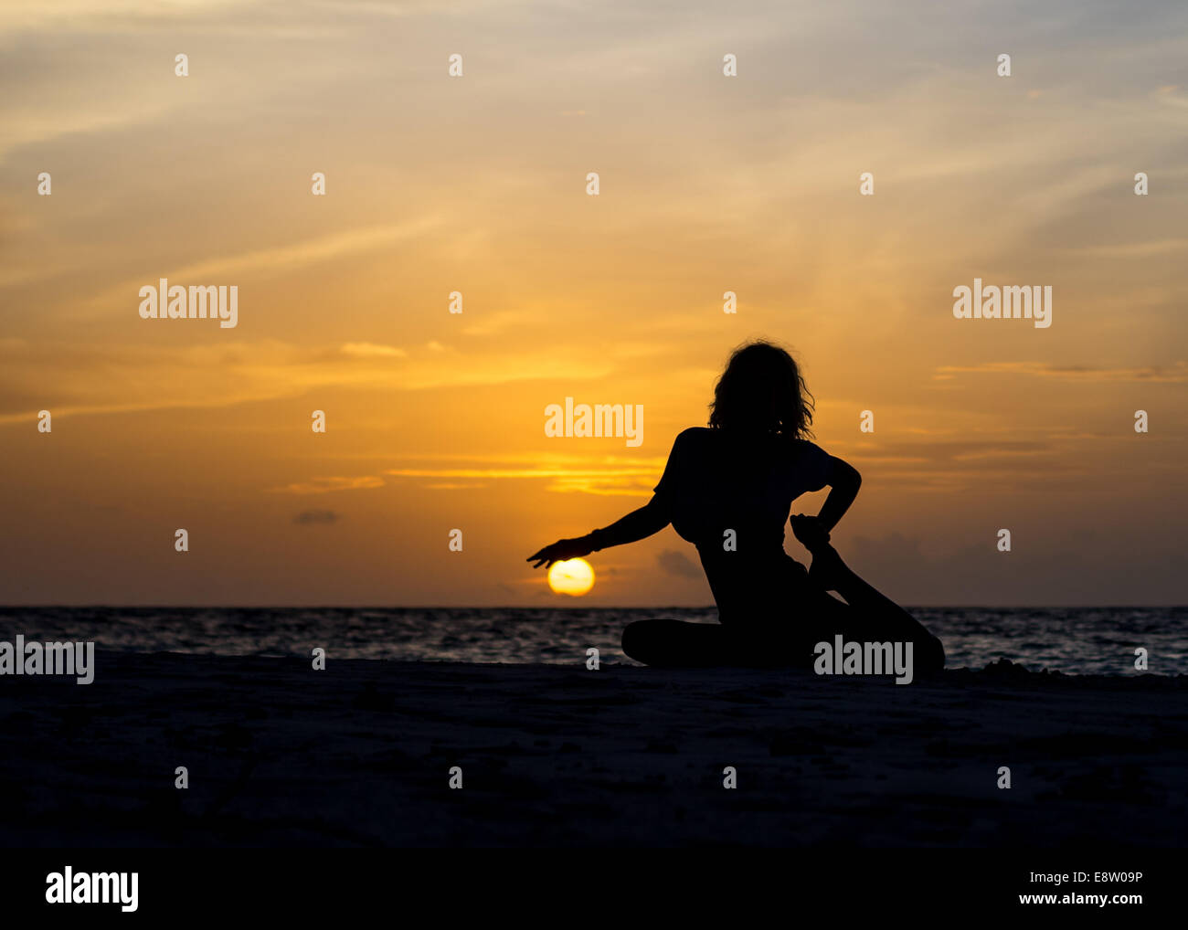 Yoga donna seduta sulla costa del mare al tramonto Foto Stock