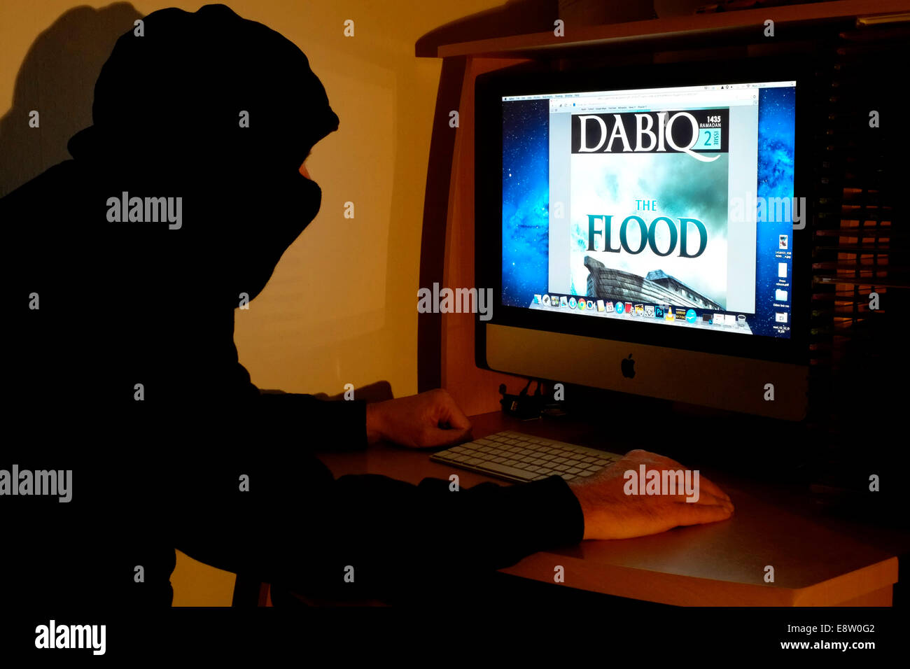 Incappucciato e uomo mascherato seduto al suo computer la lettura della versione on line di uno stato islamico terrorista dabiq magazine Foto Stock