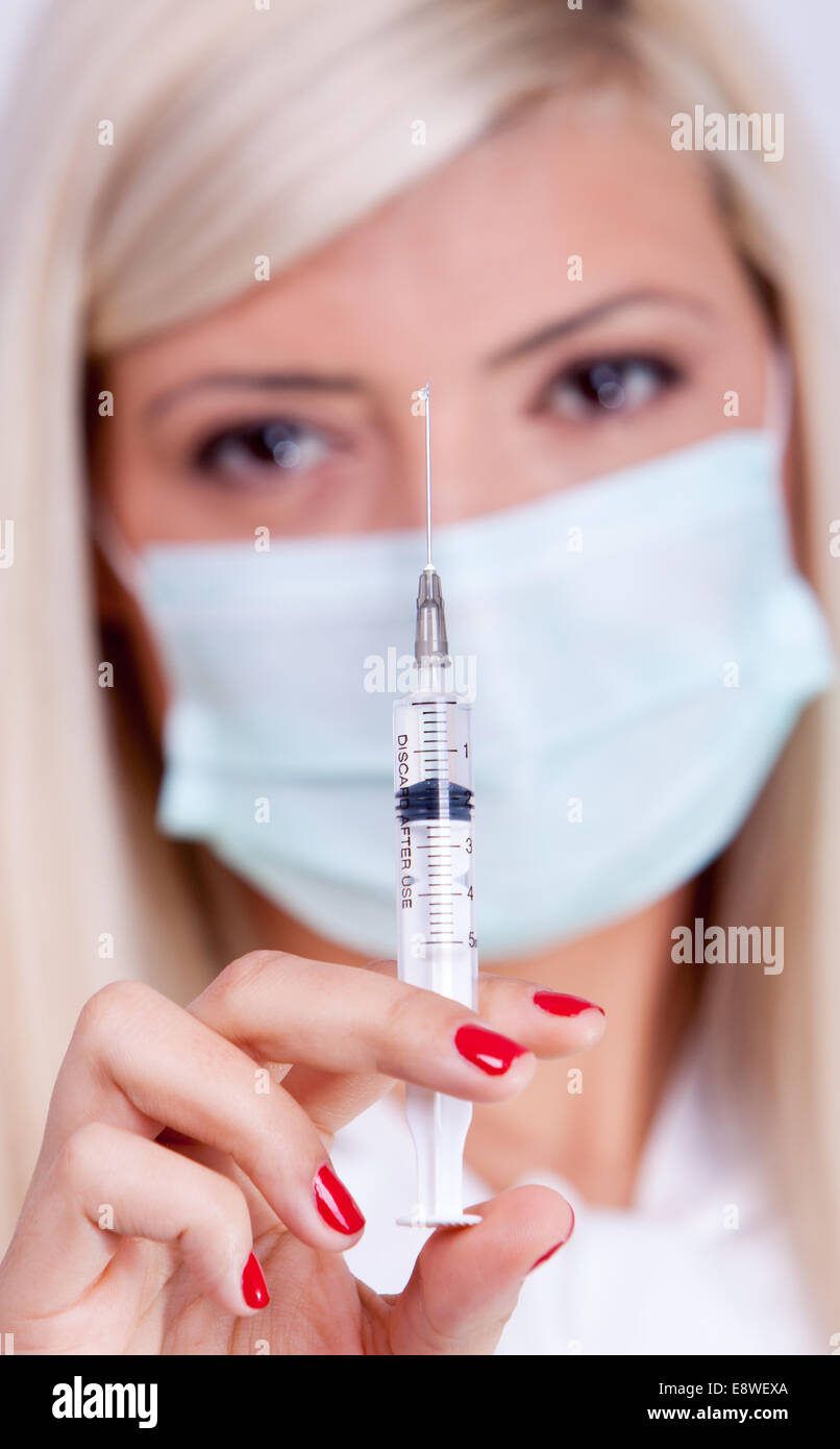 Donne medico o infermiere in maschera medico tenendo la siringa di iniezione Foto Stock
